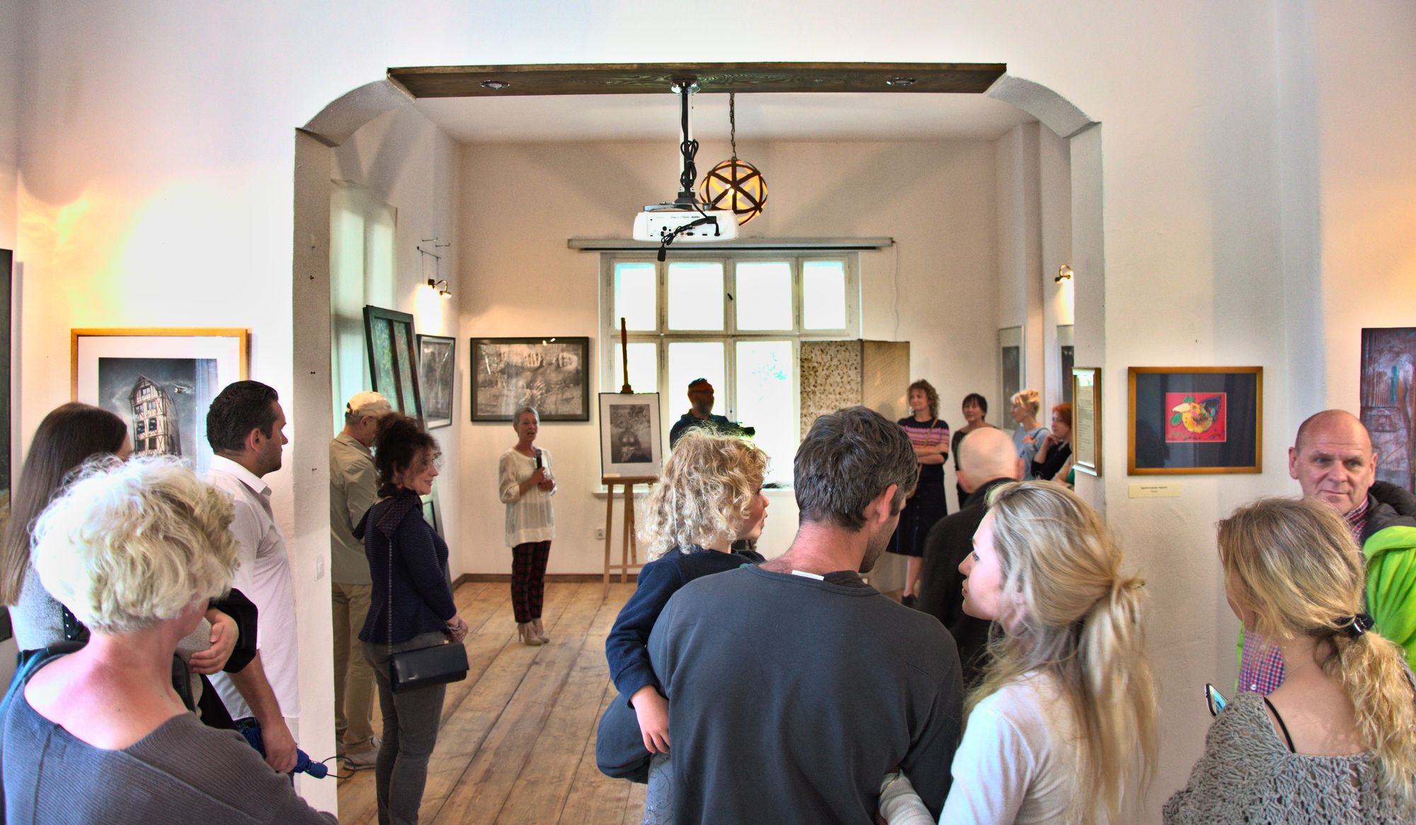 Widzowie w galerii oglądają wystawę obrazów rozwieszonych na ścianach Sudeckiego Centrum Kultury i Sztuki