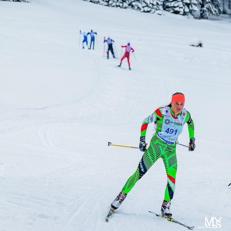 Narciarka biegnąca na nartach w zawodach na tle śnieżnej łąki