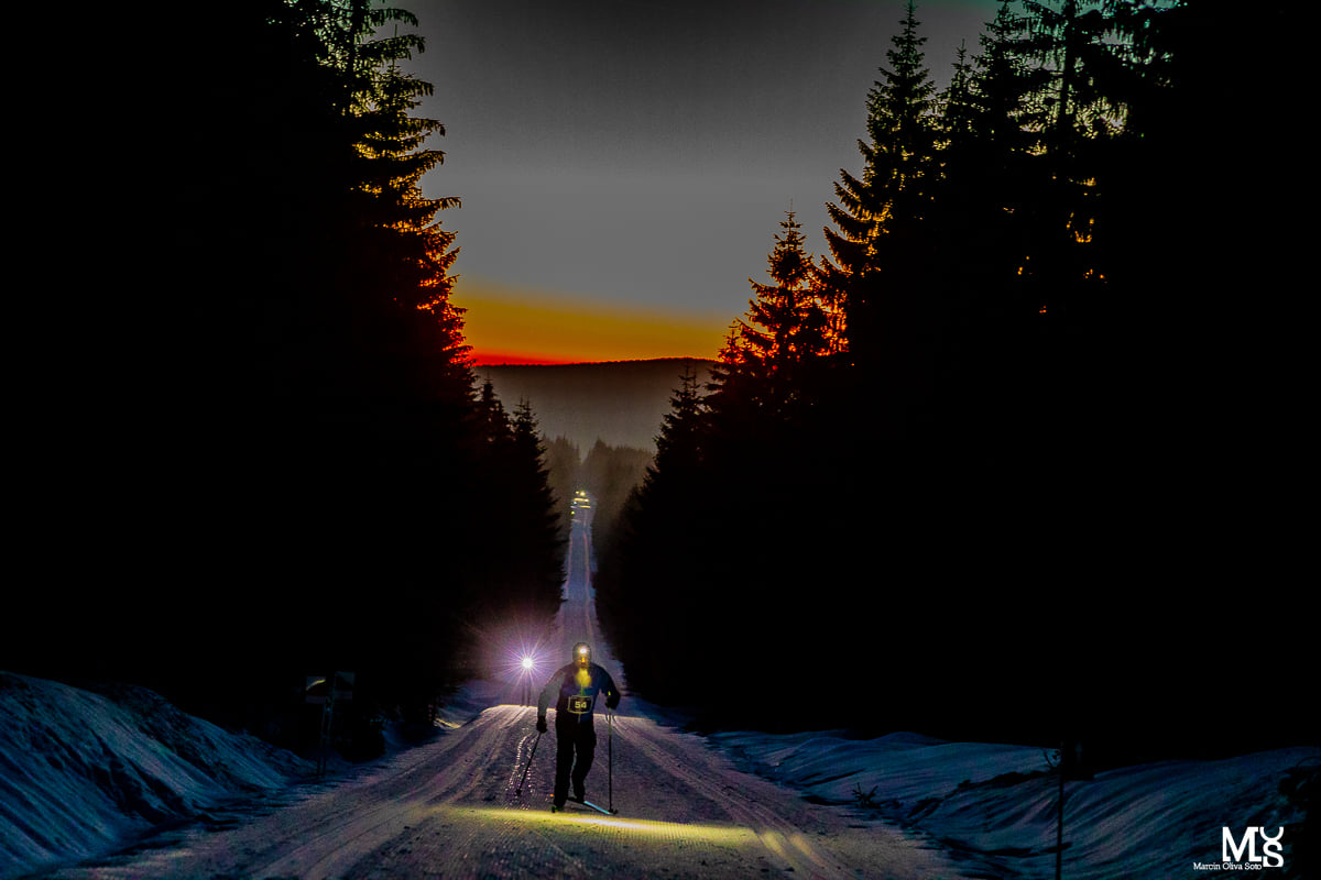 Trasa narciarska w lesie i biegacze na nartach oświetlający ją latarkami czołowymi